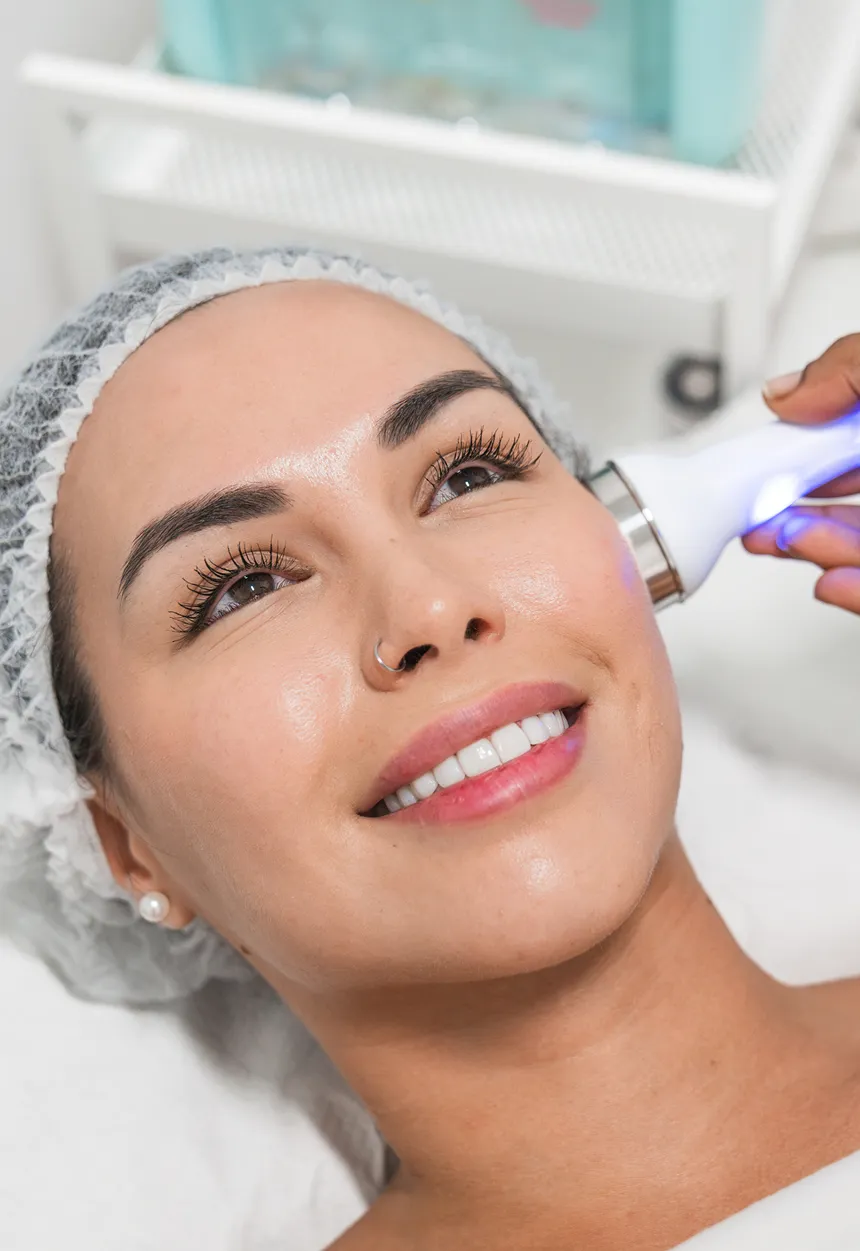 Woman wearing a dress and a cap on her head, while receiving a laser treatment on her face