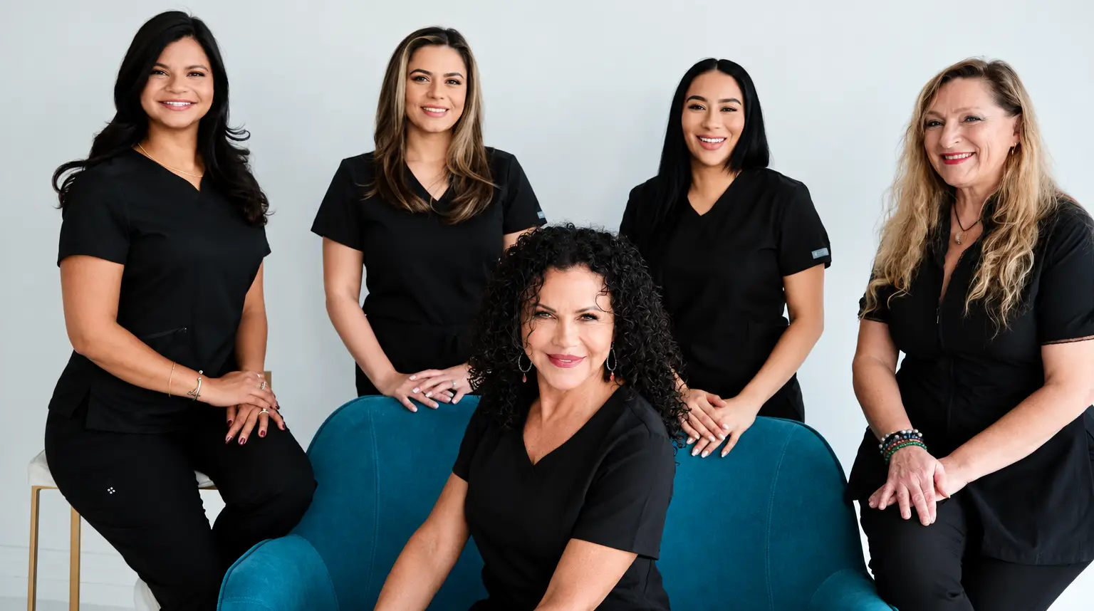 Group of women in scrubs sitting on a blue couch in front of a white wall