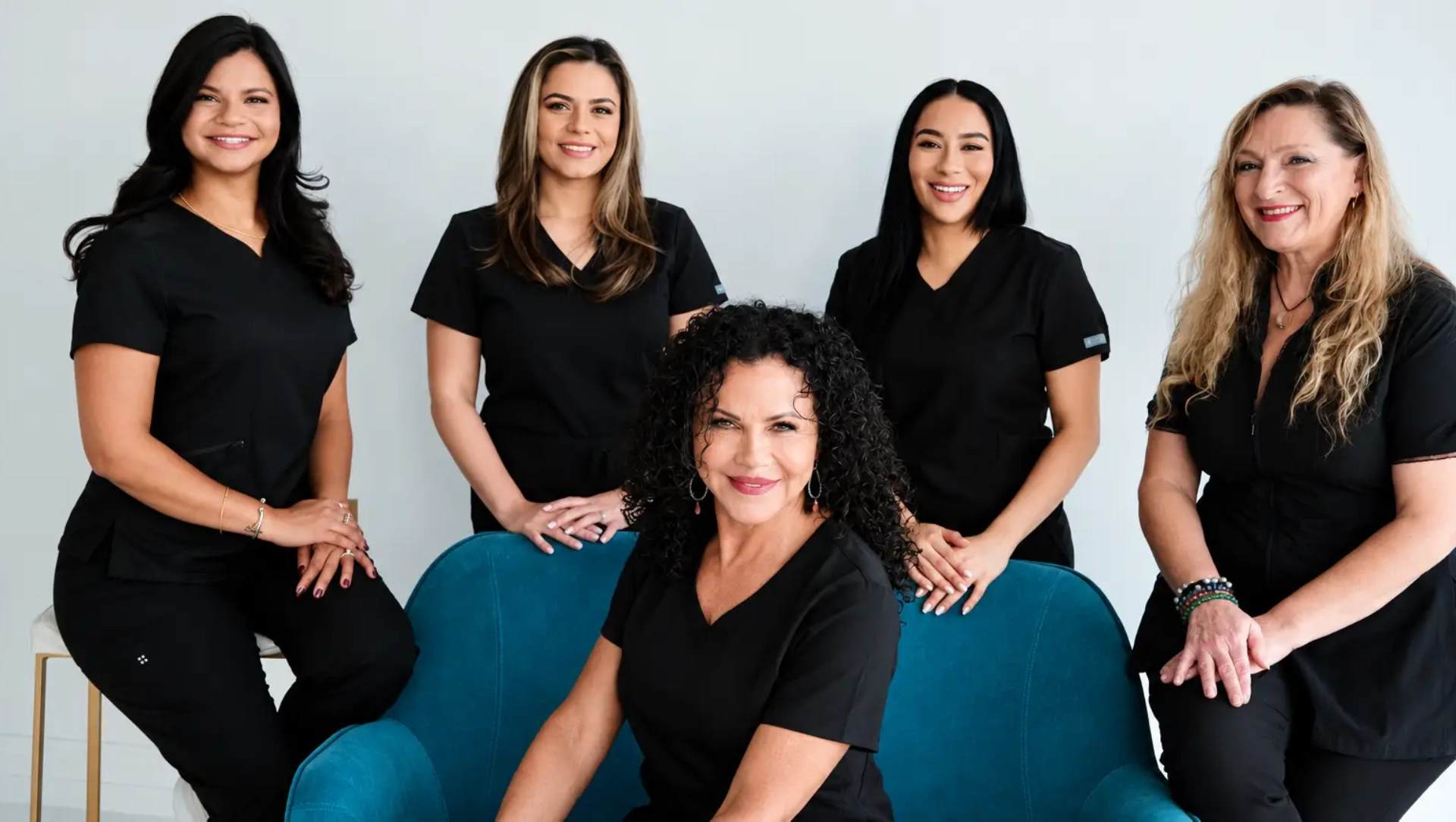 Group of women in scrubs sitting on a blue couch in front of a white wall