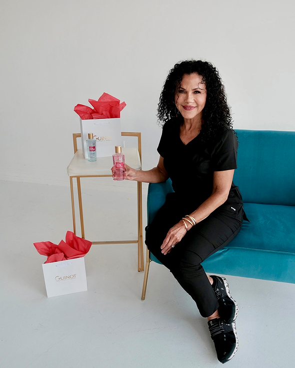 Woman sitting on a blue couch with a bottle of perfume in her hand, surrounded by a table